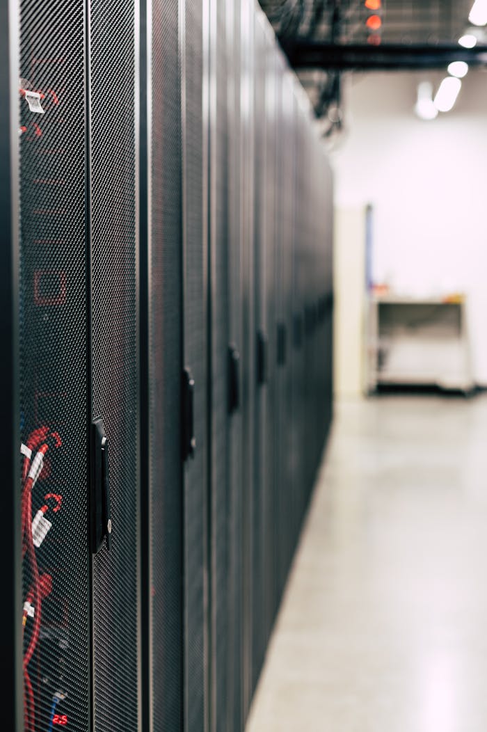 about-us Metal black cabinets with servers inside with red wires connected standing in row in lighted room